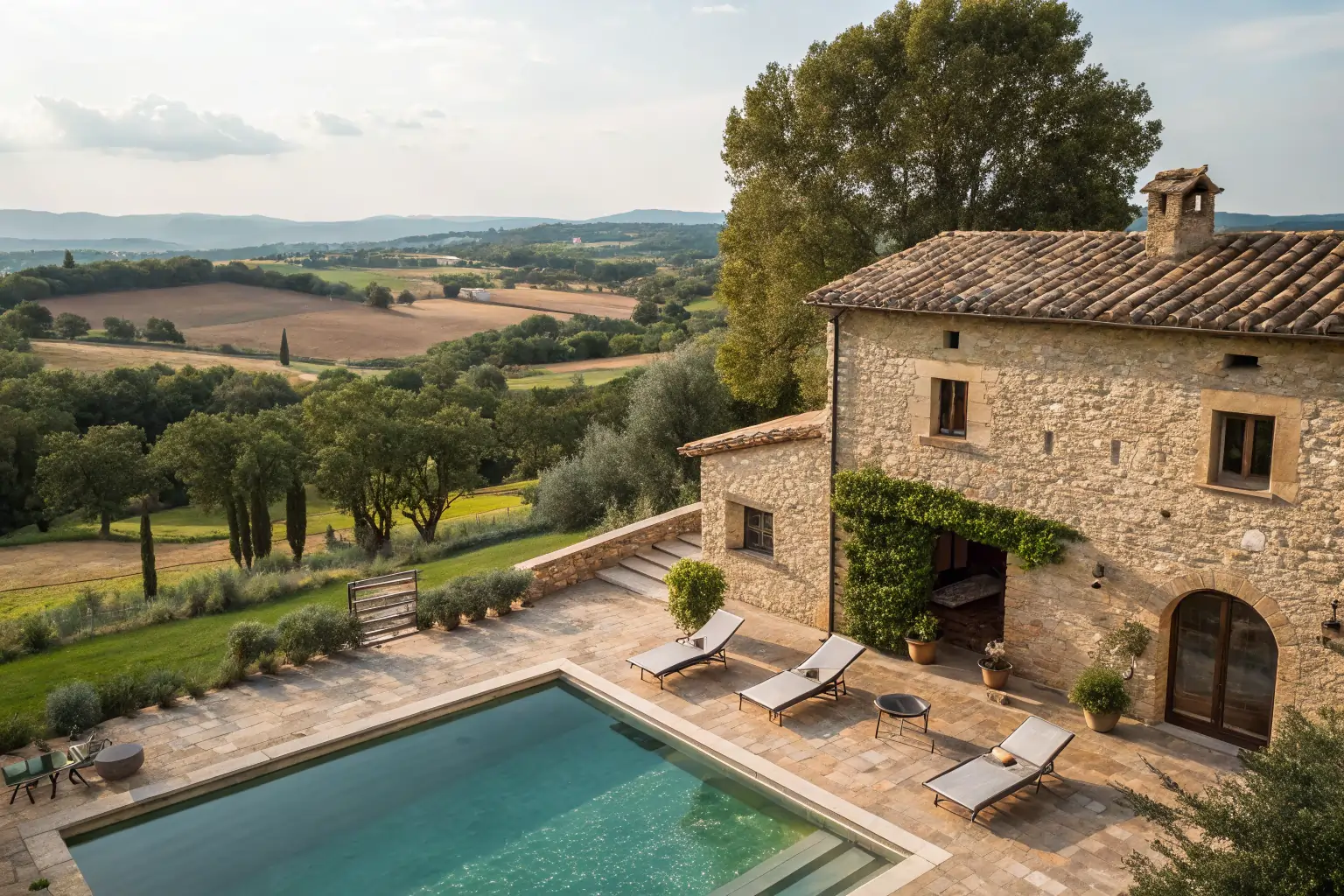 Esta imagen captura la esencia de Mas La Casassa, un refugio rural cerca de Sant Gregori, Girona. Se muestra una piscina privada junto a una construcción de piedra tradicional, con tumbonas sobre suelo de terracota, árboles y campo al fondo.suites con piscina privada